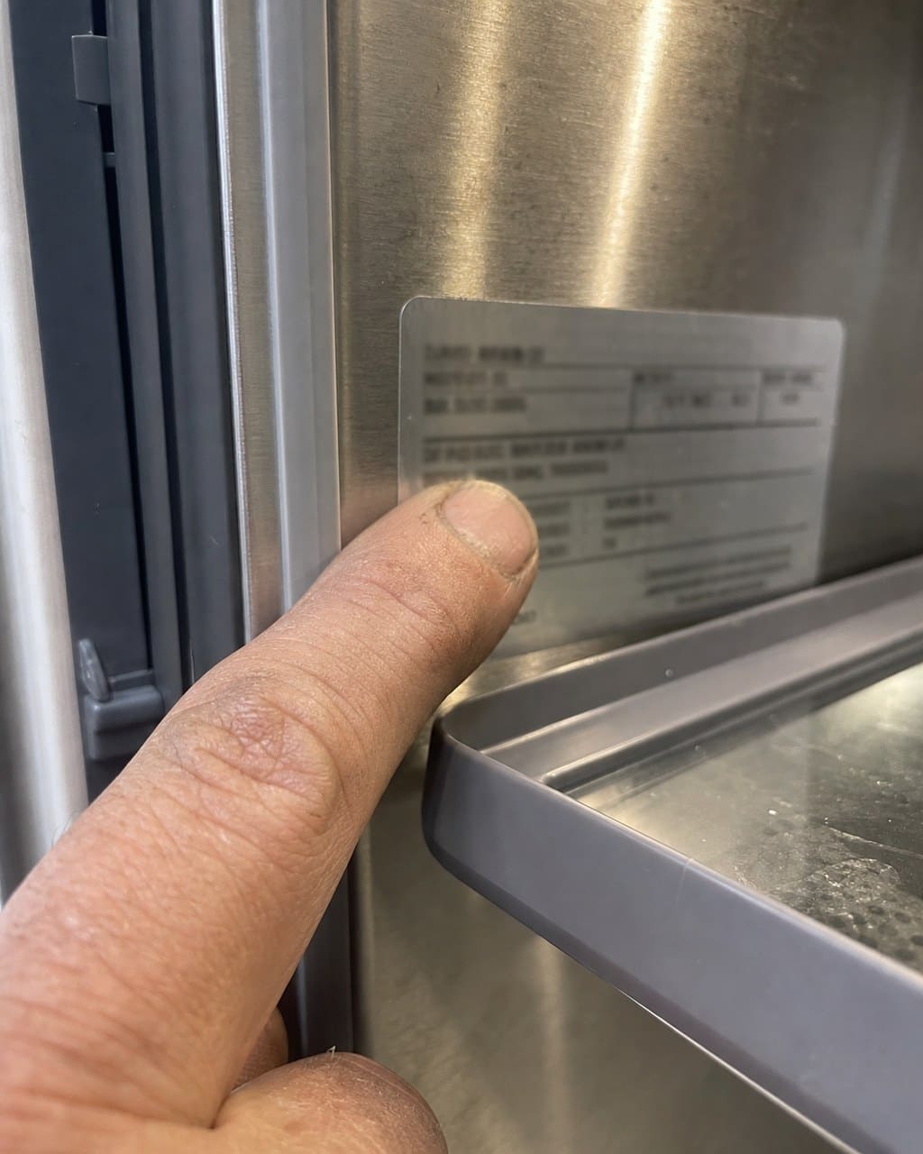 Technician pointing at the silver model and serial number sticker inside a Sub-Zero refrigerator